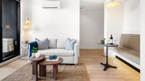 A modern living room with a white sofa, a round coffee table, and a small side table with a bottle and glasses. - Cozy 1BR Melbourne Escape | Balcony | Pool | GYM (Melbourne)
