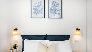 A neatly made bed with a dark headboard, two framed botanical prints on the wall, and bedside lamps on either side. - Cozy 1BR Melbourne Escape | Balcony | Pool | GYM (Melbourne)