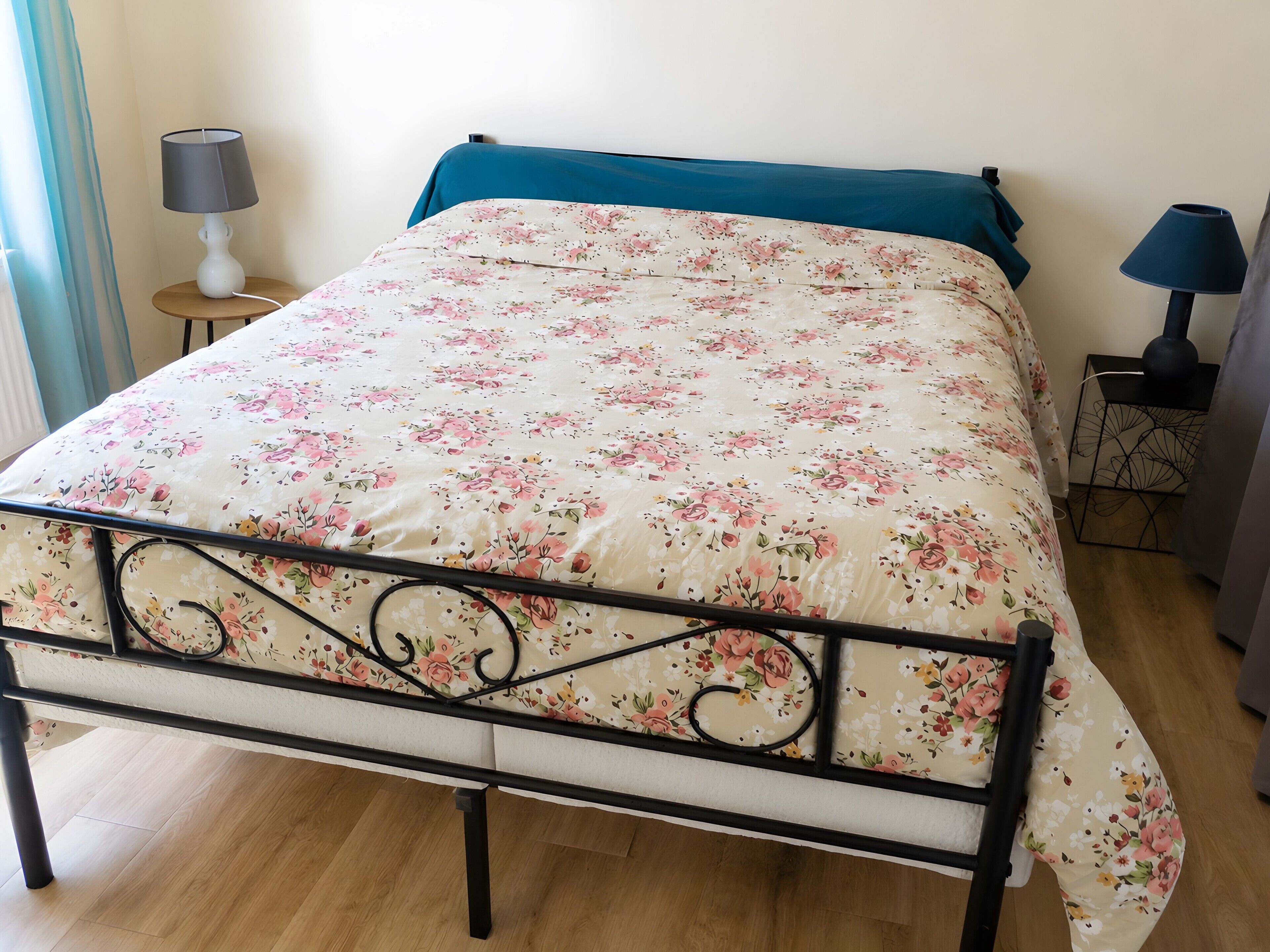 A bed with a floral bedspread, a blue pillow, and a metal frame. There are two bedside tables with lamps.