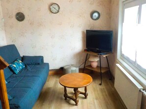 A living room with a blue sofa, a wooden coffee table, a television on a stand, and two wall clocks. - Holiday Home 'Gite618' (Helfaut)
