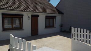 A white building with a tiled roof, a door, and windows. There is a white fence with a gate, and a table with a cable on it. - Holiday Home 'Gite618' (Helfaut)