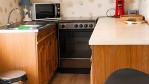 A compact kitchen with wooden cabinets, a microwave, a stove, and a trash bin. - Holiday Home 'Gite618' (Helfaut)