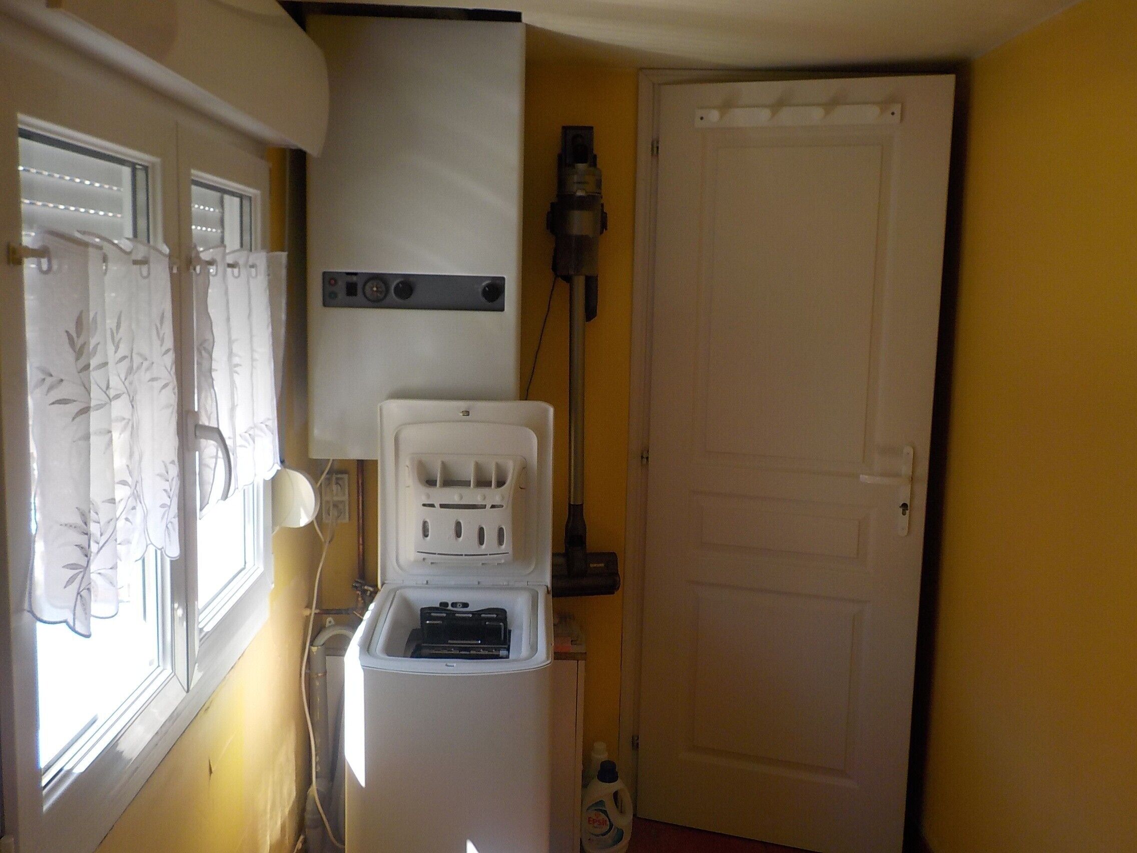 Une petite pièce équipée d’un lave-linge, d’un aspirateur et d’une porte.