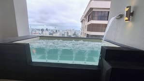 Ein moderner Poolbereich im Innenbereich mit Blick auf die Stadt, inklusive eingebautem Whirlpool und einer Wandleuchte.