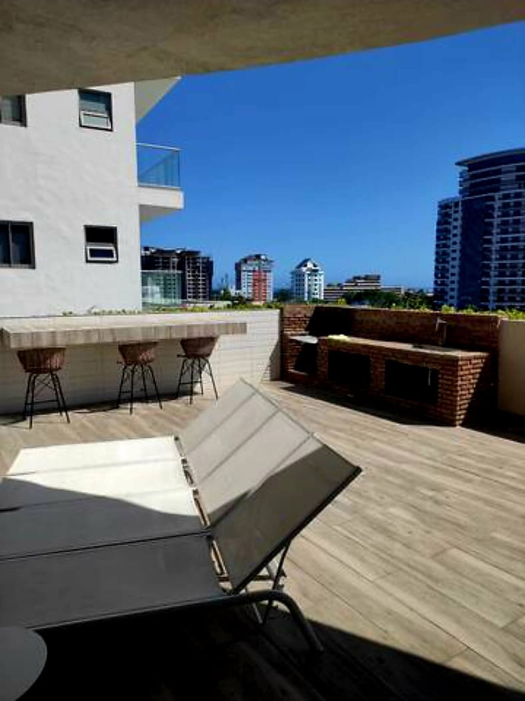 Eine Terrasse im Freien mit Tisch und Stühlen, ein gemauerter Grill und Blick auf eine Stadtlandschaft.