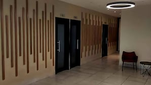 Ein moderner Flur mit Fliesenboden, Holzlatten an der Wand und runden Deckenleuchten.
