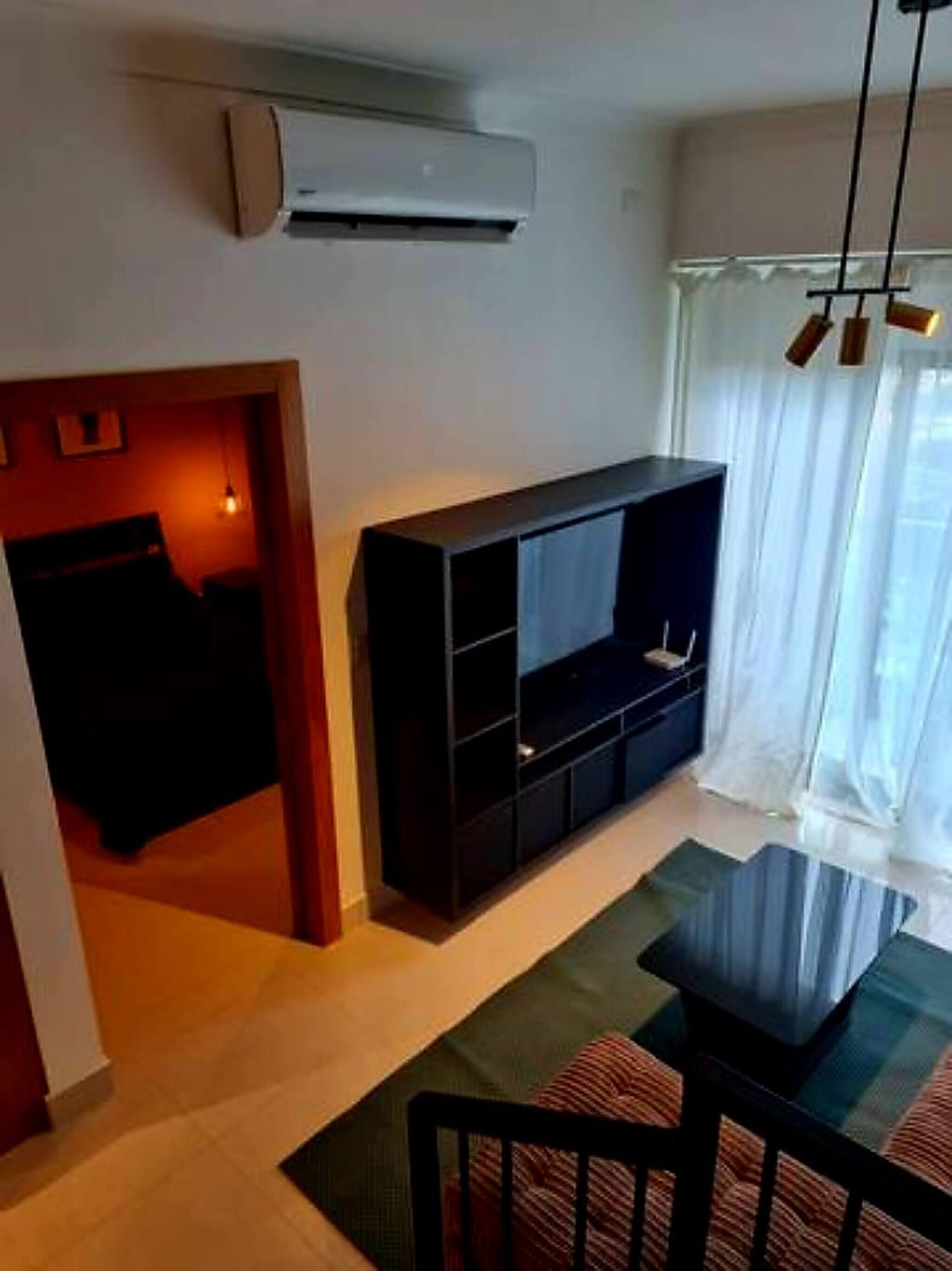 A modern living room with a black entertainment unit, a glass coffee table, and a dining table with chairs.