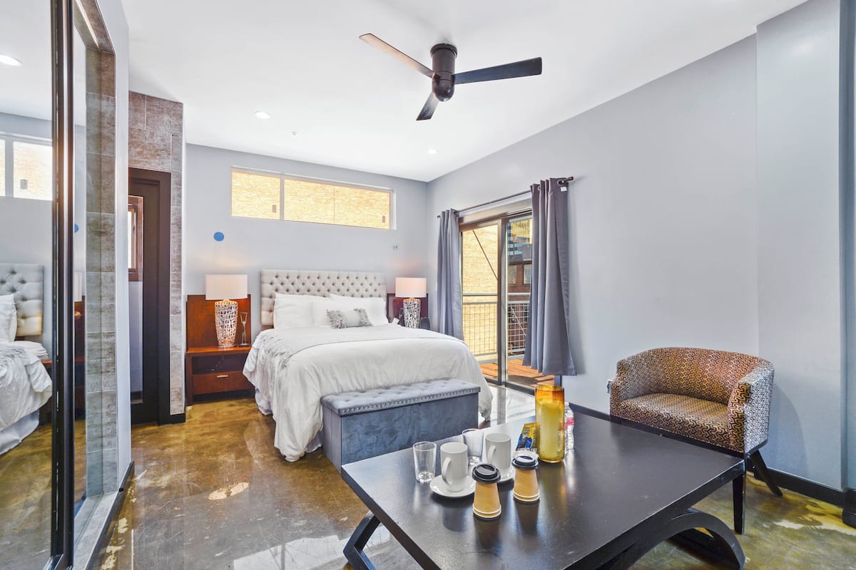A hotel room with a bed, a dining table with breakfast items, a chair, and a window with curtains.