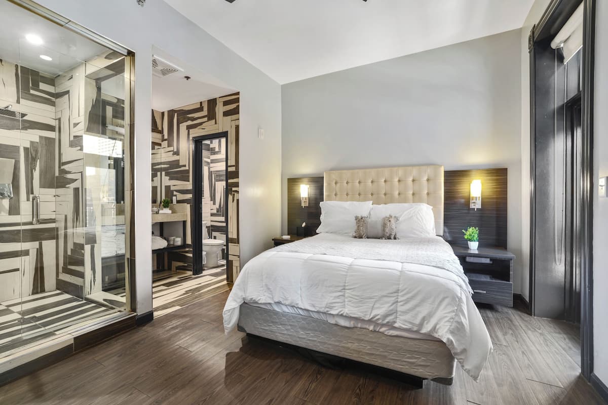 A modern bedroom with a large bed, a glass partition, and a wooden floor.