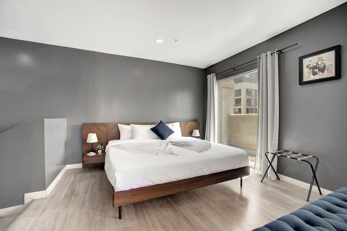 A modern bedroom with a large bed, a nightstand, a small table, and a view of the city through the window.