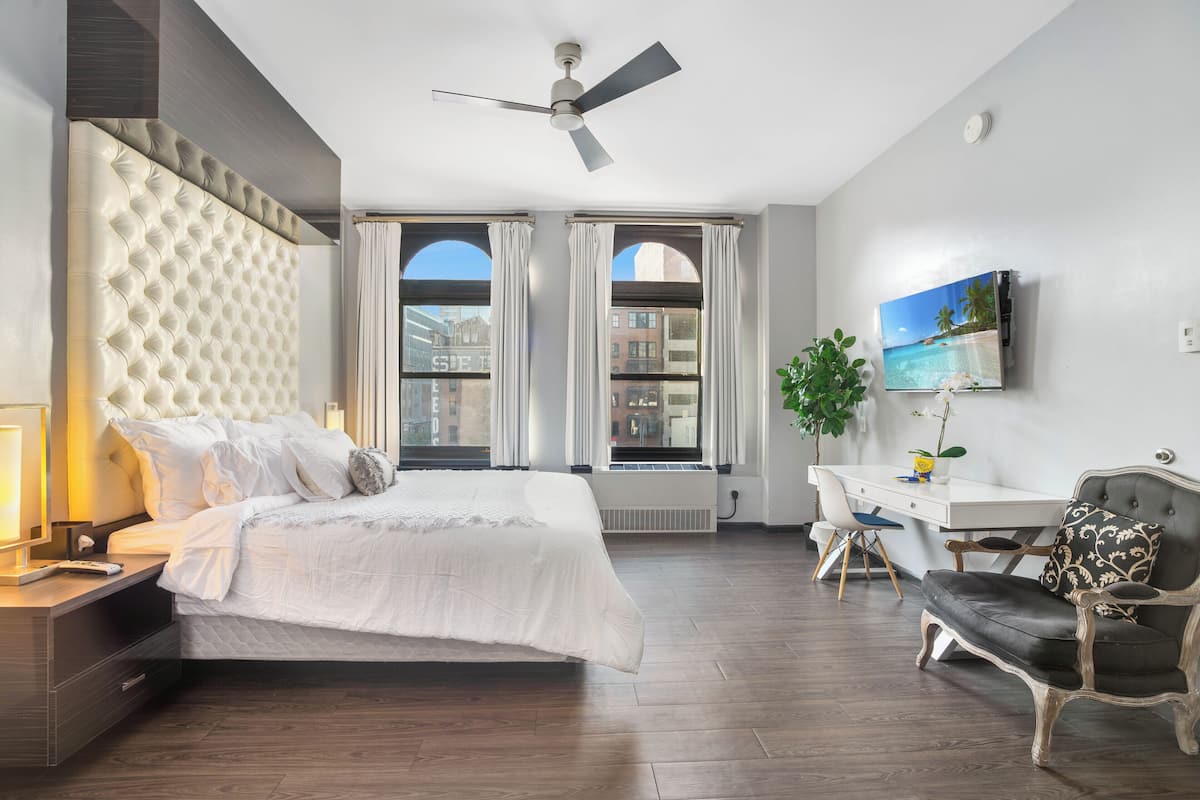 A bedroom with a large bed, a desk, a chair, a ceiling fan, and a window with curtains.