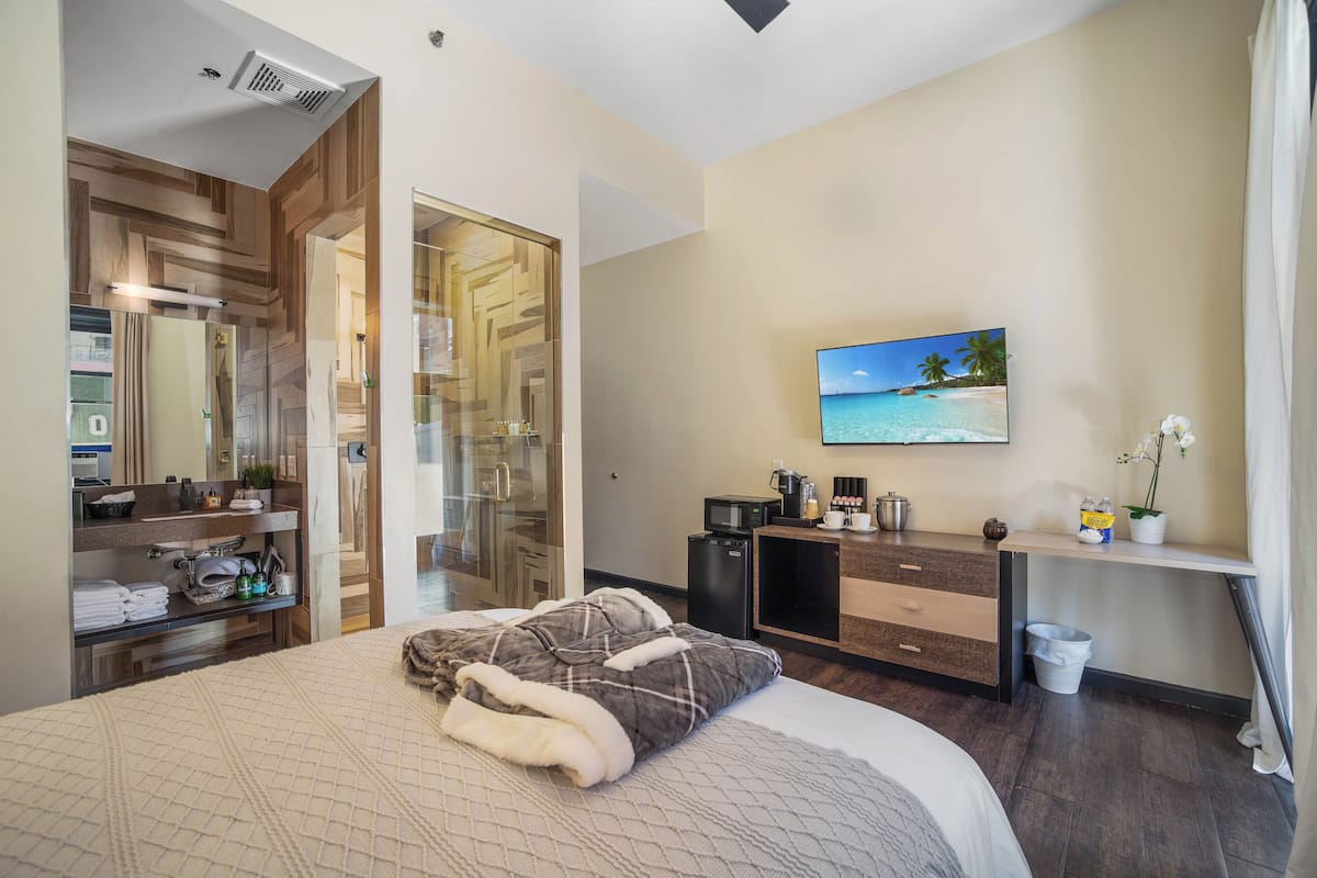A modern hotel room with a bed, a TV, a desk, and a bathroom.