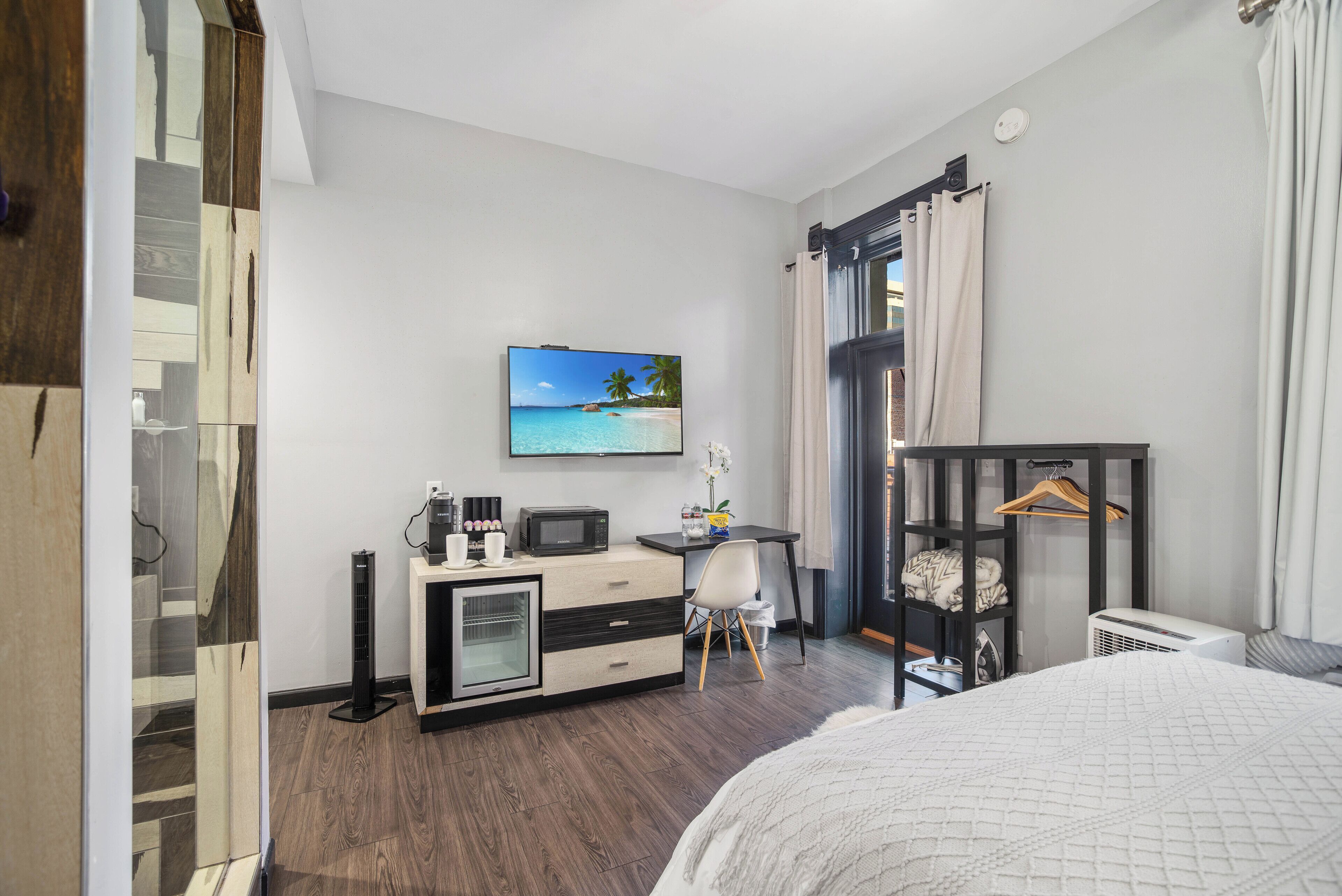Une chambre d’hôtel moderne équipée d’un lit, d’un bureau avec un ordinateur, d’un téléviseur diffusant des images d’une plage tropicale et d’une armoire avec un miroir.