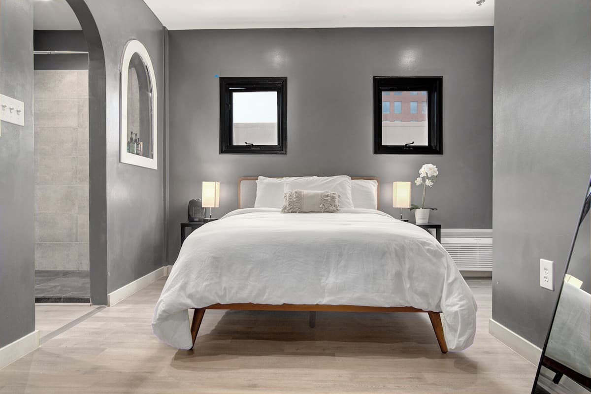A modern bedroom with a large bed, two bedside tables, a nightstand, a potted orchid, and two framed pictures on the wall.