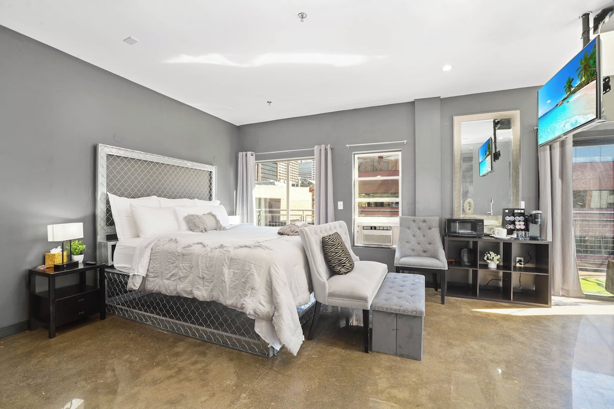 A modern bedroom with a large bed, a seating area, a television, and a view of the outdoors.