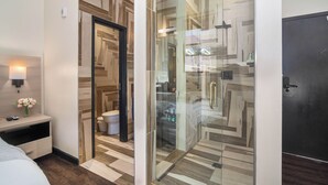 A modern bathroom with a glass shower enclosure, a wooden vanity, and a bedside table with a lamp and flowers. - Good Hotels Downtown Denver (Denver)