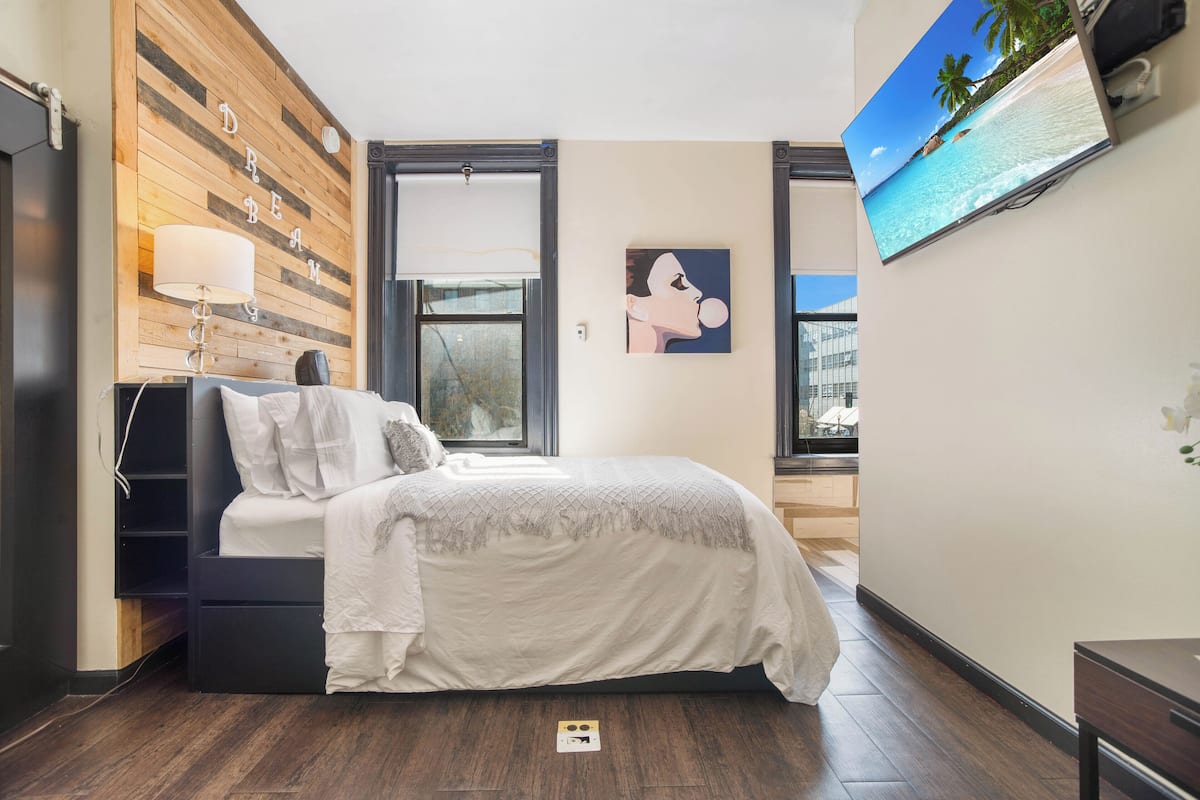 A bedroom with a bed, a TV, a wooden wall, and a window.