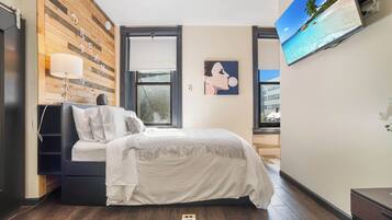 A bedroom with a bed, a TV, a wooden wall, and a window.