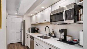 Een moderne keuken met witte kasten, een magnetron, een koffieapparaat en een spoelbak.