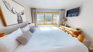 Ein geräumiges Schlafzimmer mit einem großen Bett, einem Nachttisch aus Holz, einem Schreibtisch und einem Fenster mit Vorhängen.