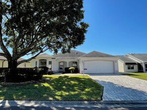 A residential house with a garage, a well-maintained lawn, and a large tree in the foreground. - Your happy place just minutes from Spanish Springs (The Villages)
