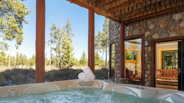 A hot tub with a stone wall backdrop and a view of a forest. - 144 Rainbow - Fairways at Pole Creek 6 beds, private outdoor HT, heated garage (Tabernash)
