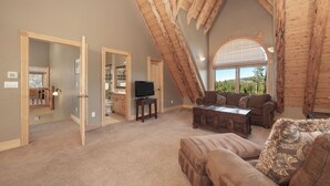 A spacious loft bedroom with a high ceiling, wooden beams, a large window, a television, and a cozy seating area. - 144 Rainbow - Fairways at Pole Creek 6 beds, private outdoor HT, heated garage (Tabernash)