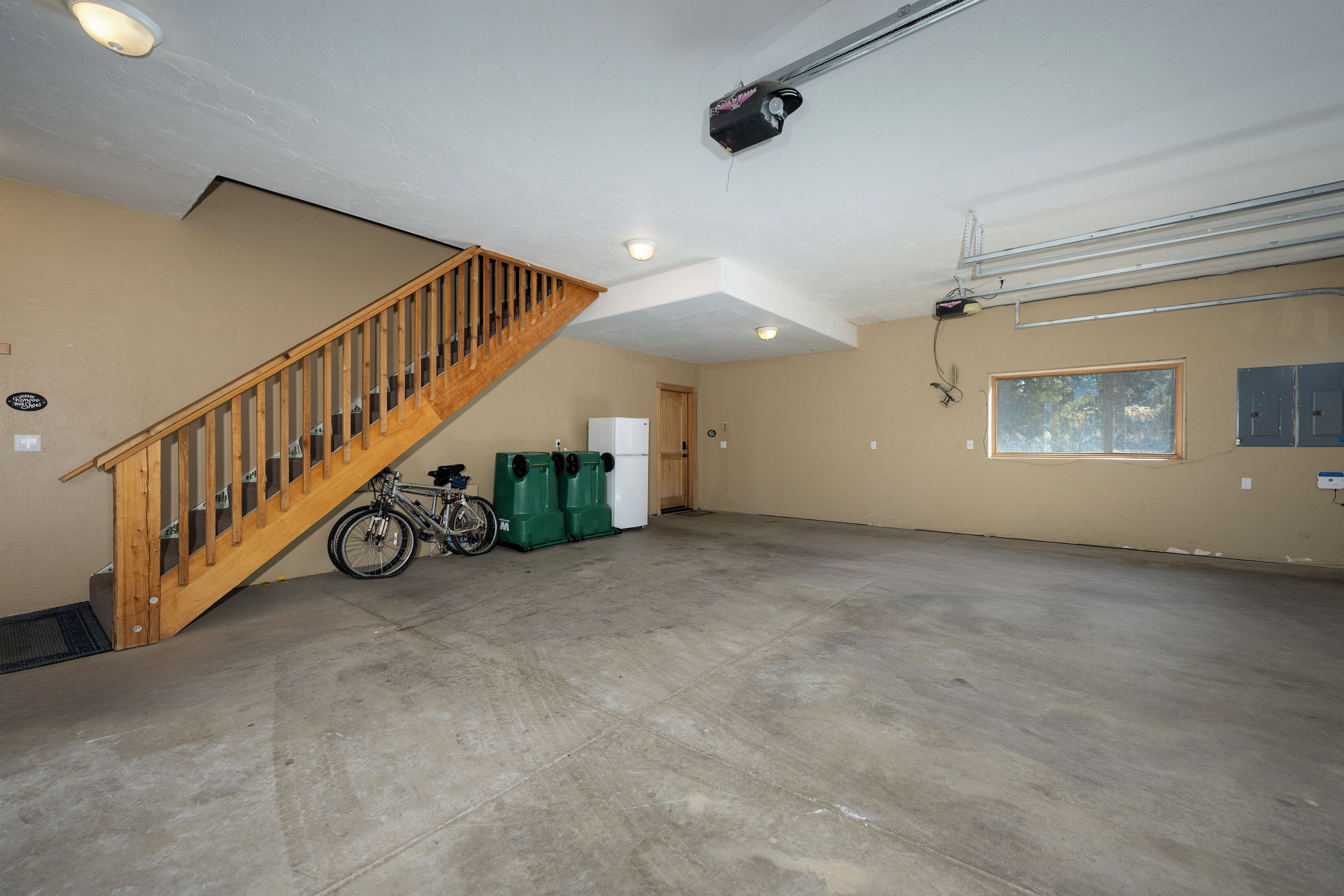 Een ruime garage met een houten trap, een fiets en groene opbergbakken.