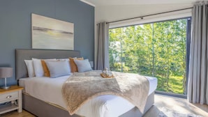 Ein modernes Schlafzimmer mit einem großen Bett, einem Nachttisch, einer Fensterbank und Blick auf Grünfläche.