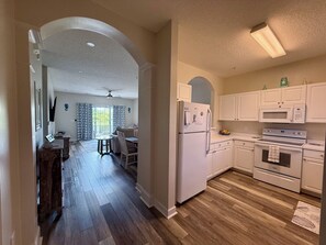 A kitchen with white cabinets, a refrigerator, a microwave, and an oven. There is a dining area with a table and chairs. - White Shores-Quiet 2BR/2BA Condo + Pool's near beach in North Myrtle Beach SC (North Myrtle Beach)