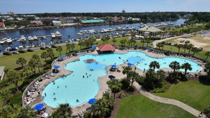 Ein großer Poolkomplex im Freien mit mehreren Pools, umgeben von Palmen und einem Hafen im Hintergrund.