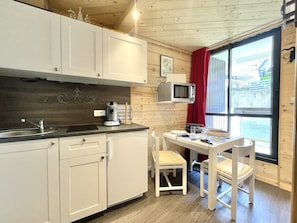A compact kitchen with white cabinets, a microwave, and a dining table with chairs. - Studio Altitude 1850 – Ski-in/Ski-out – L (Les Menuires)