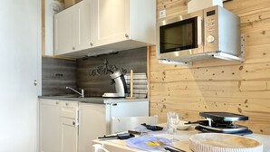 Een compacte keuken met witte kastjes, een magnetron, een waterkoker en een eettafel voor twee personen.