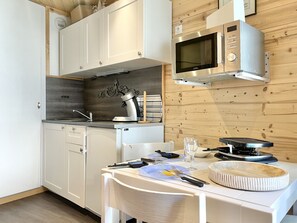 A compact kitchen with white cabinets, a microwave, a kettle, and a dining table set for two. - Studio Altitude 1850 – Ski-in/Ski-out – L (Les Menuires)