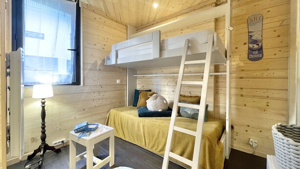 Een gezellige kamer met een stapelbed, een trapje, een klein tafeltje met een lamp en een raam.