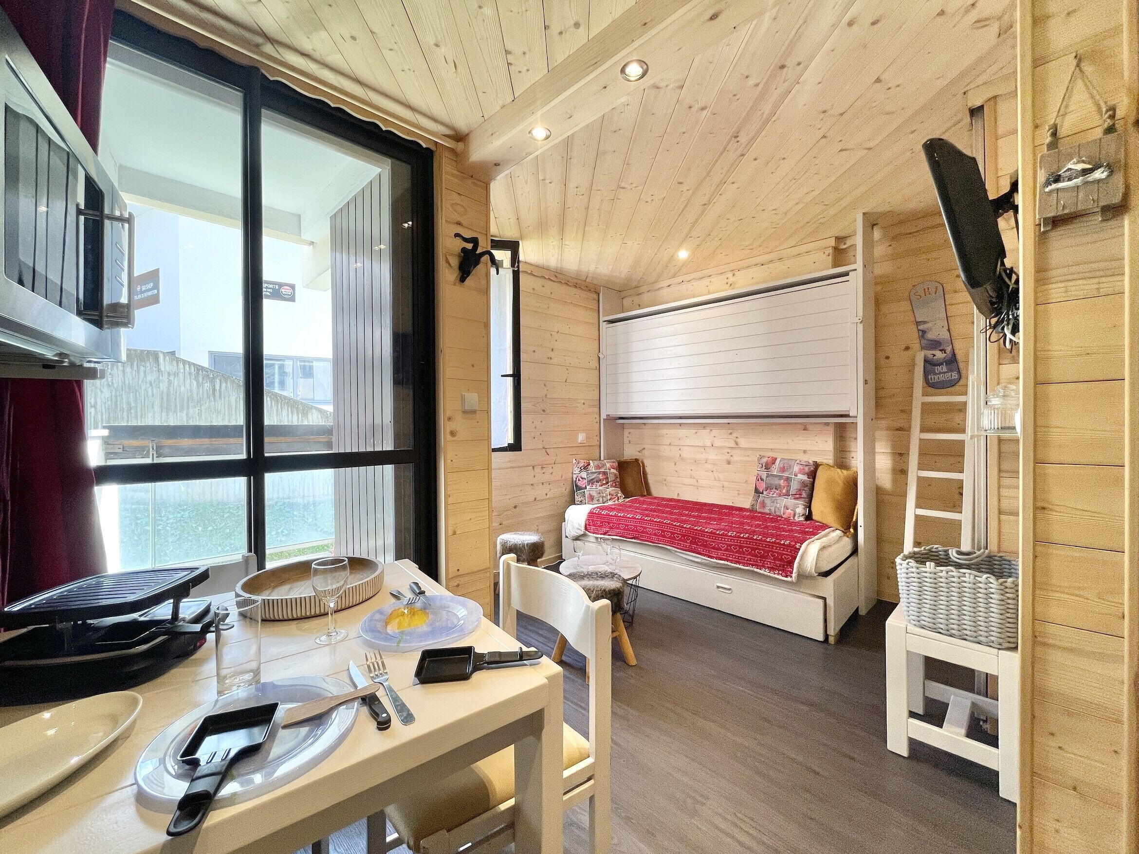 A cozy room with a bed, a dining table with cutlery, and a window.