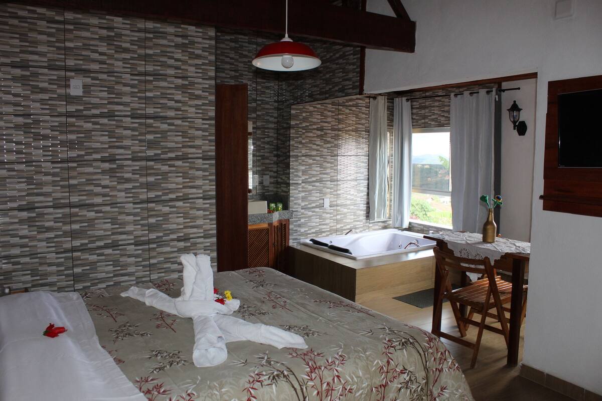 Een hotelkamer met een bed, een badkamer, een eethoek en uitzicht op de omgeving.