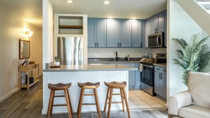 A modern kitchen with a central island, bar stools, and a dining area. - Charming Renovated Condo w/Loft & Golf Views near Ritz-Carlton Turtle Bay (Kahuku)