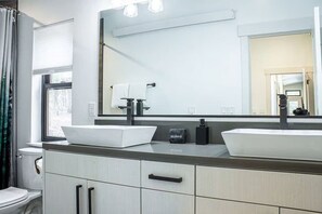 Ein modernes Badezimmer mit zwei Aufsatzwaschbecken, einem großen Spiegel und einem Fenster mit Vorhängen.