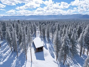 Eine Hütte, umgeben von einem dichten Wald mit schneebedeckten Bäumen.