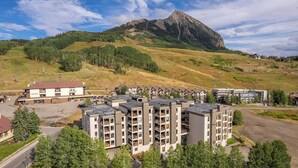 A multi-story hotel with a central courtyard, surrounded by a hilly landscape and a prominent mountain in the background. - Plaza 536 | Shuttle to Crested Butte Lifts | Hot Tubs+Sauna | 2BR Sleeps 6 (Crested Butte)