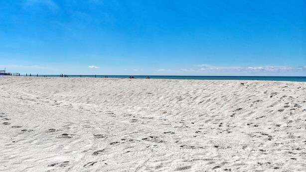 Ein weiter Sandstrand mit Fußspuren, die zum Wasser führen.