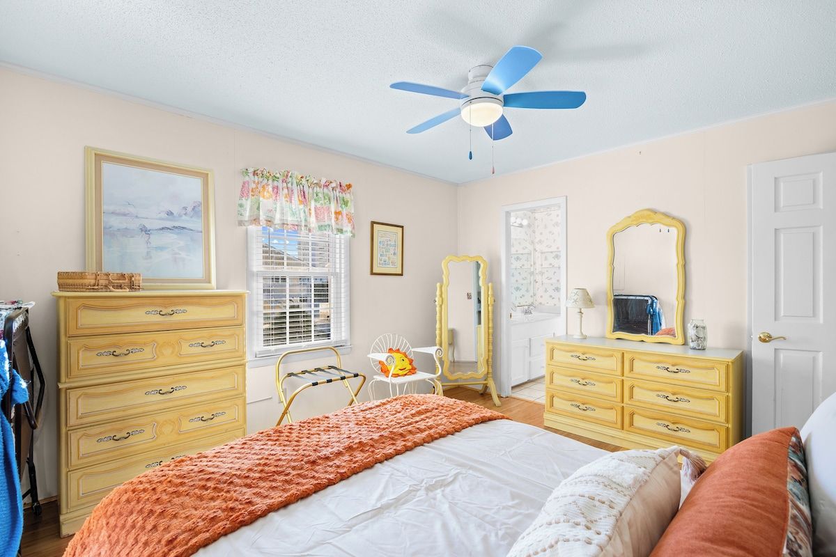 Une chambre à coucher comprenant un lit, une commode, un miroir et un ventilateur de plafond.