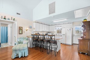 A kitchen with white cabinets, a wooden countertop, and a dining area with a bar stool and chairs. - 4 Bedroom Home in Cherry Grove, 1 Block From Beach (North Myrtle Beach)