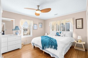 A bedroom with a bed, a dresser, a nightstand, a ceiling fan, and a window with curtains. - 4 Bedroom Home in Cherry Grove, 1 Block From Beach (North Myrtle Beach)