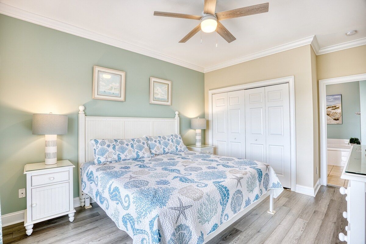 A bedroom with a bed, nightstands, a ceiling fan, and a door.