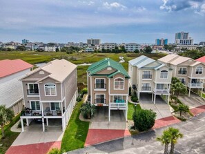 A residential area with multi-story houses, a green roof on one house, and a clear sky. - Sea House 5 bedroom w/pool (North Myrtle Beach)