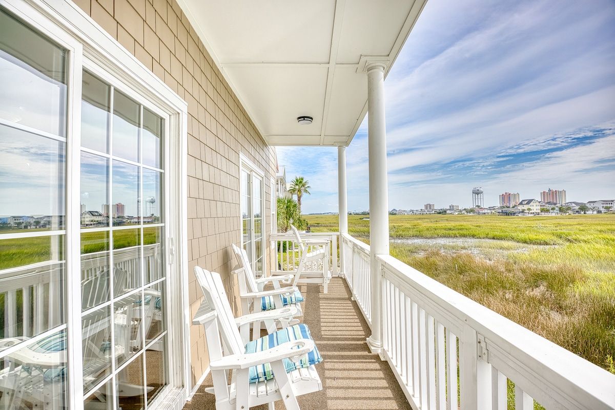 A covered porch with white chairs and a view of a cityscape.