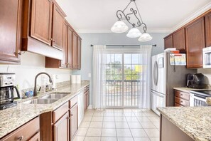 A kitchen with granite countertops, wooden cabinets, a stainless steel refrigerator, and a coffee maker. - Sea House 5 bedroom w/pool (North Myrtle Beach)