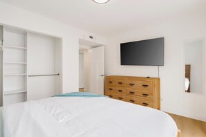 Une chambre à coucher comprenant un lit, une armoire, un téléviseur et une porte donnant sur une autre pièce.